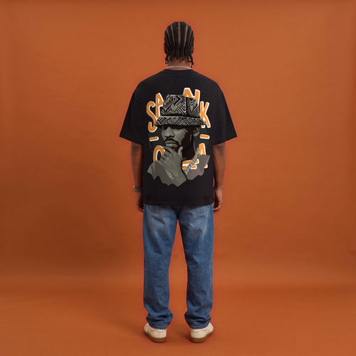 Blackness Sankofa King Tee, black, worn by a model — back view, Sankofa woven hat portrait print, terracotta backdrop