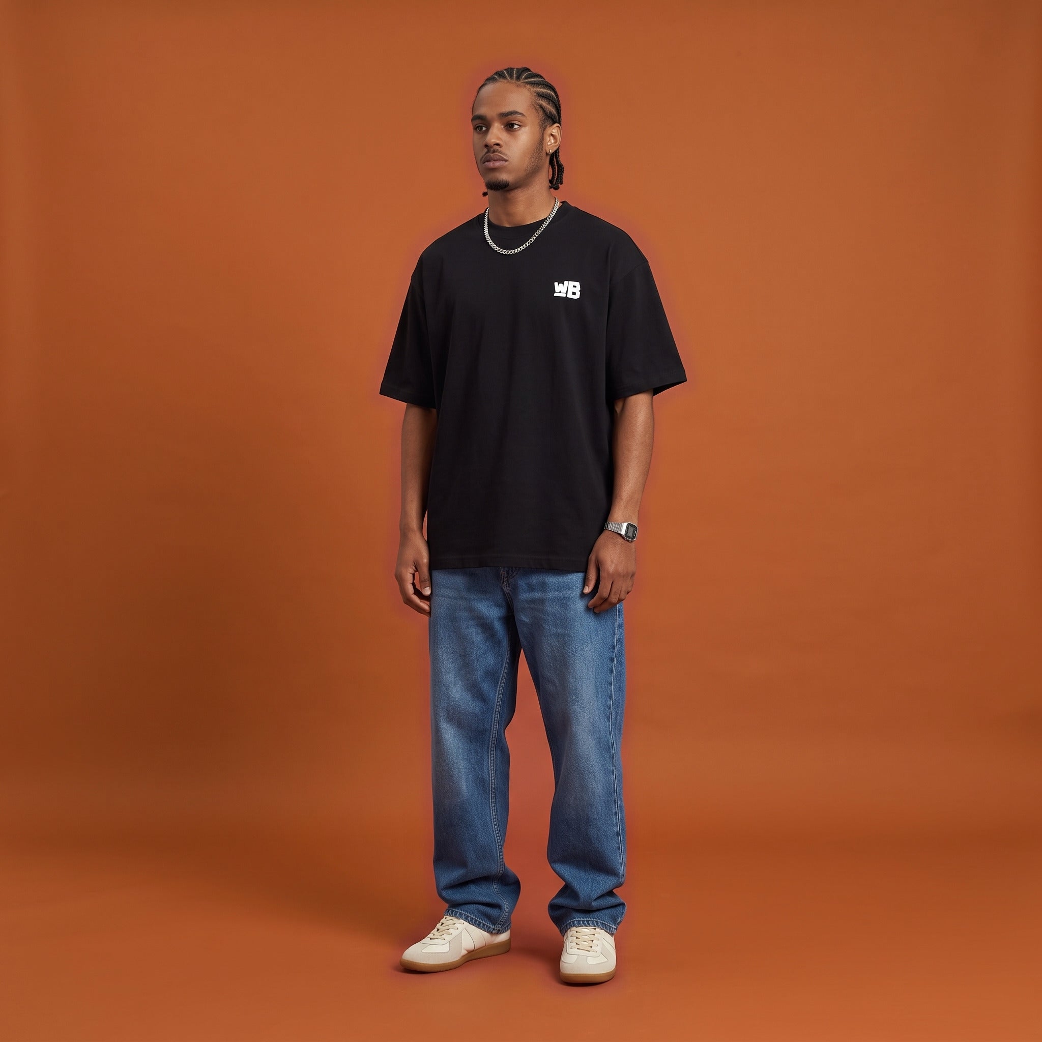 Blackness Sankofa King Tee, black, worn by a model — front view with WB chest logo, burnt-orange terracotta studio backdrop