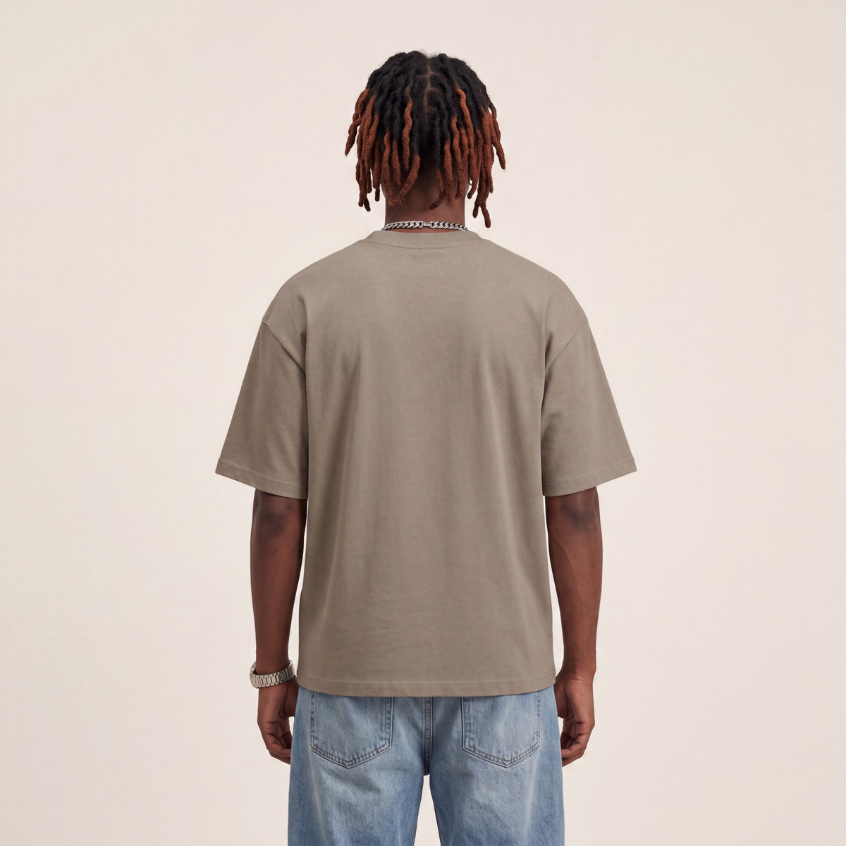 Base Blackness Tee Brown worn by model, back view showing the clean plain back on warm ivory studio backdrop
