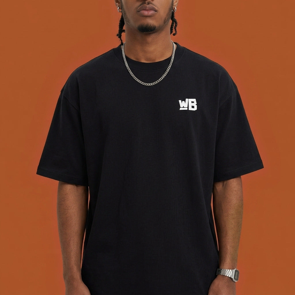 Blackness Sankofa King Tee, black — chest detail close-up with WB monogram and ribbed collar, terracotta backdrop