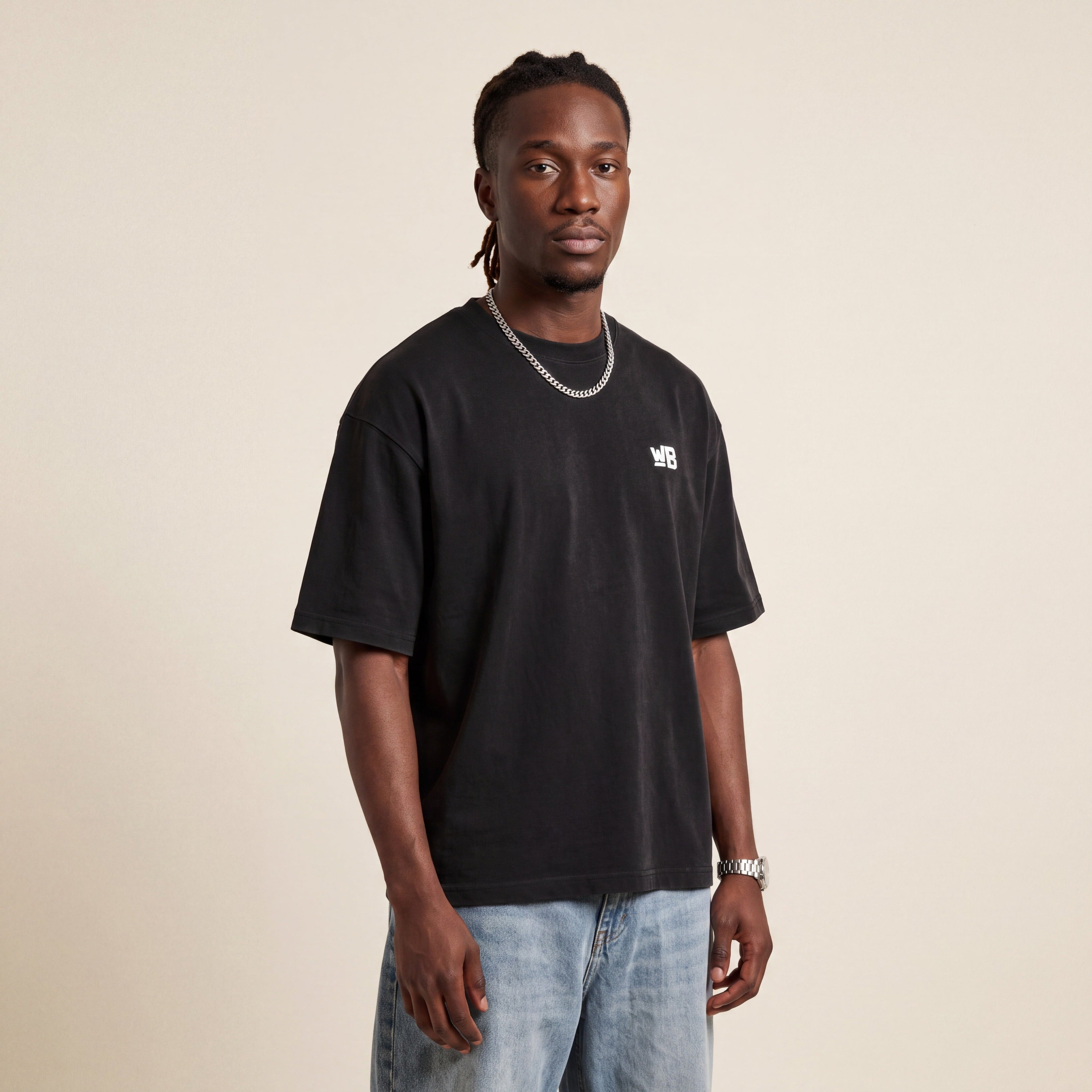 Base Blackness Tee Black worn by model, front view with WB chest logo on warm ivory studio backdrop
