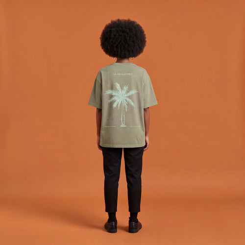 Blackness Libation Tee, brown khaki, worn by a model — back view, palm tree Libation print, terracotta-orange studio backdrop