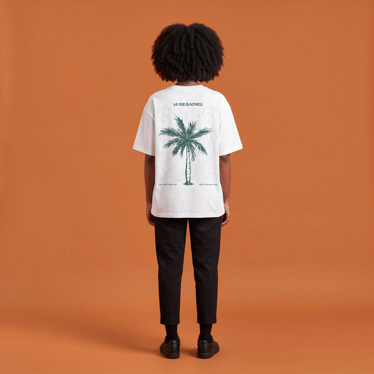 Blackness Libation Tee, white, worn by a model — back view, palm tree Libation print, terracotta-orange studio backdrop