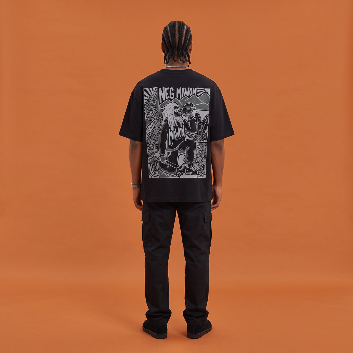 Blackness Mawon Tee, black, worn by a model — back view, Neg Mawon conch-blower block print, terracotta-orange studio backdrop