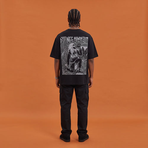 Blackness Mawon Tee, black, worn by a model — back view, Neg Mawon conch-blower block print, terracotta-orange studio backdrop