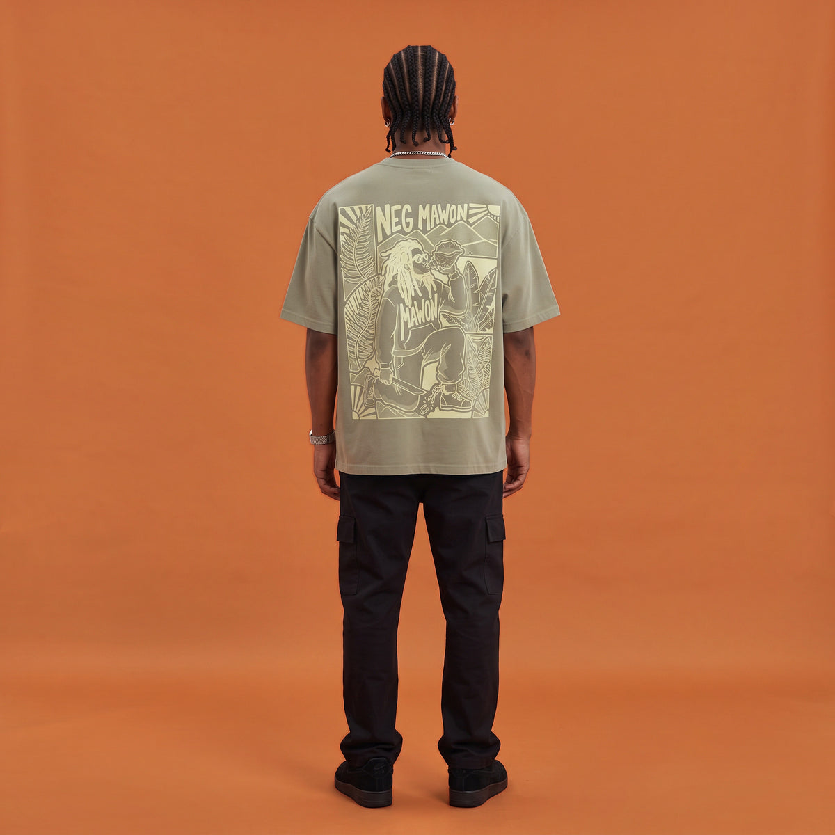 Blackness Mawon Tee, brown khaki, worn by a model — back view, Neg Mawon conch-blower block print, terracotta-orange studio backdrop