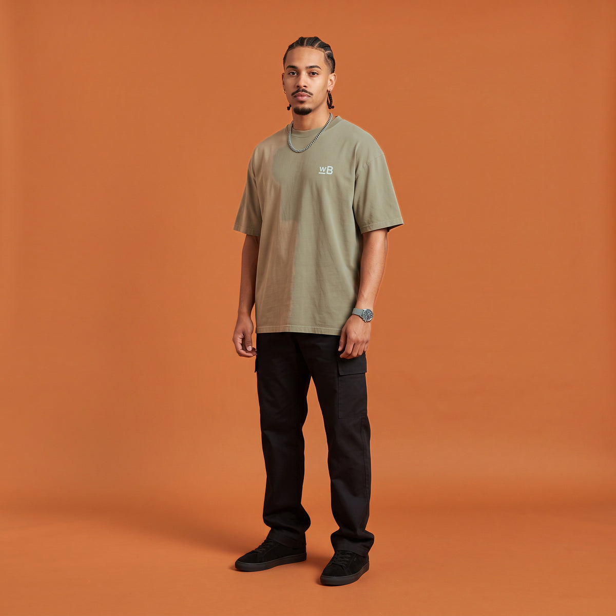 Blackness Mawon Tee, brown khaki, worn by a model — front view with WB chest logo, terracotta-orange studio backdrop