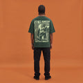 Blackness Mawon Tee, forest green, worn by a model — back view, Neg Mawon conch-blower block print, terracotta-orange studio backdrop