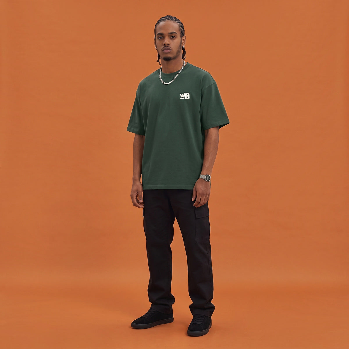 Blackness Mawon Tee, forest green, worn by a model — front view with WB chest logo, terracotta-orange studio backdrop