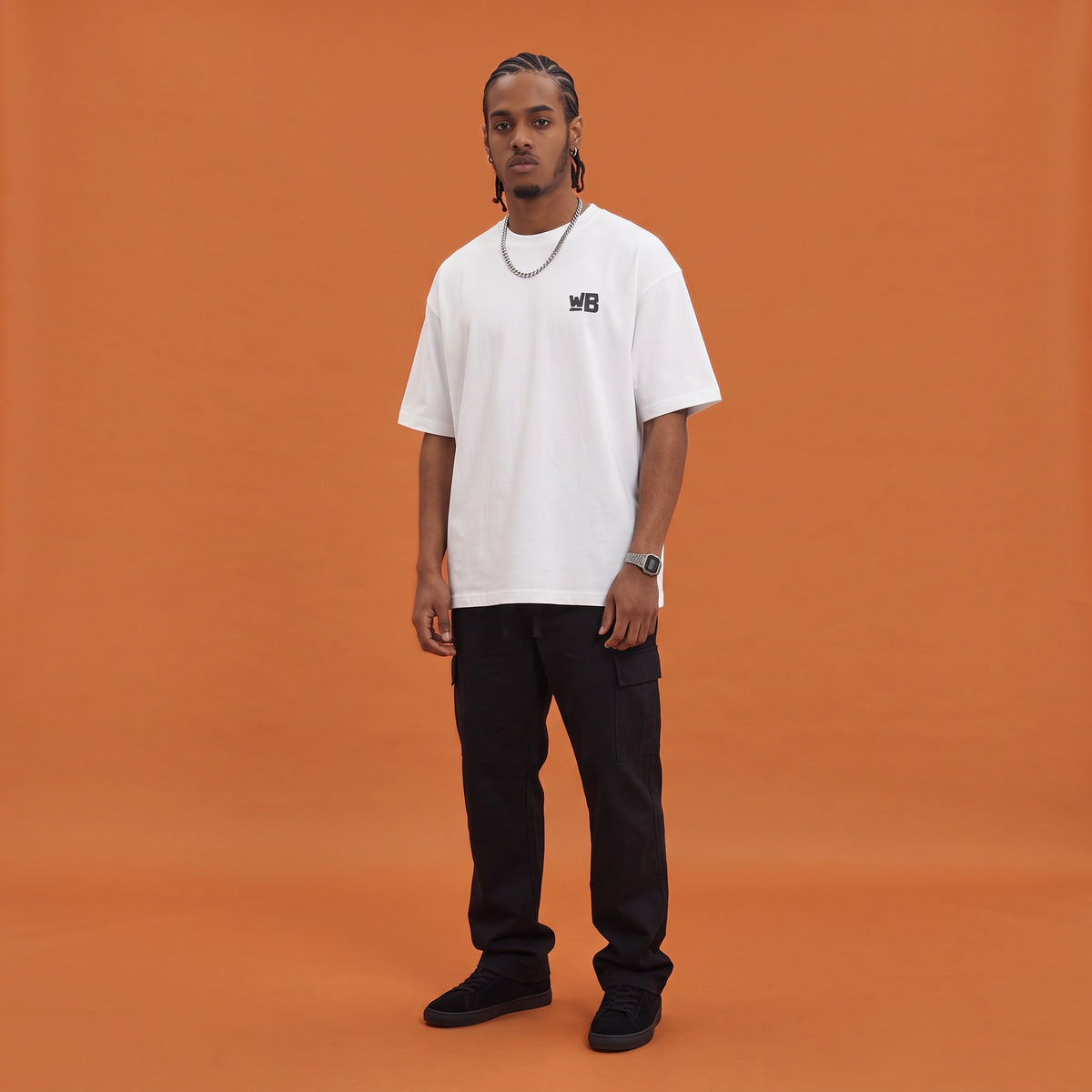 Blackness Mawon Tee, white, worn by a model — front view with WB chest logo, terracotta-orange studio backdrop