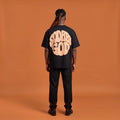 Blackness Sodabi Tee, black, worn by a model — back view, SODABI GOD bubble lettering print, terracotta-orange studio backdrop