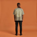 Blackness Sodabi Tee, brown khaki, worn by a model — back view, SODABI GOD bubble lettering print, terracotta-orange studio backdrop