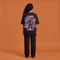 Blackness Solitude Tee, black, worn by a model — back view, Solitude portrait block print, terracotta-orange studio backdrop
