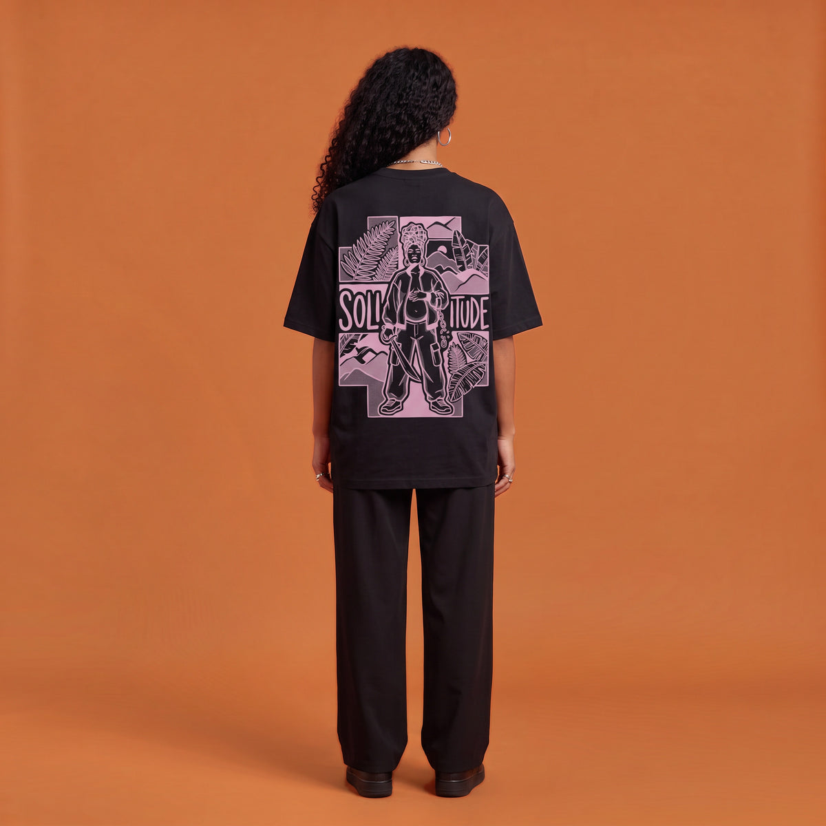 Blackness Solitude Tee, black, worn by a model — back view, Solitude portrait block print, terracotta-orange studio backdrop