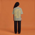 Blackness Solitude Tee, brown khaki, worn by a model — back view, Solitude portrait block print, terracotta-orange studio backdrop