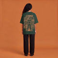 Blackness Solitude Tee, forest green, worn by a model — back view, Solitude portrait block print, terracotta-orange studio backdrop
