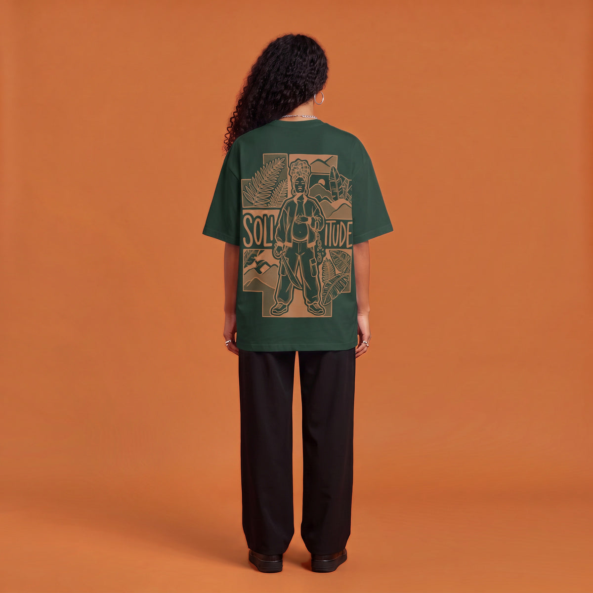 Blackness Solitude Tee, forest green, worn by a model — back view, Solitude portrait block print, terracotta-orange studio backdrop