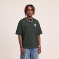 Wear Blackness Tee Green worn by model, front view with Wear Blackness chest print on warm ivory studio backdrop