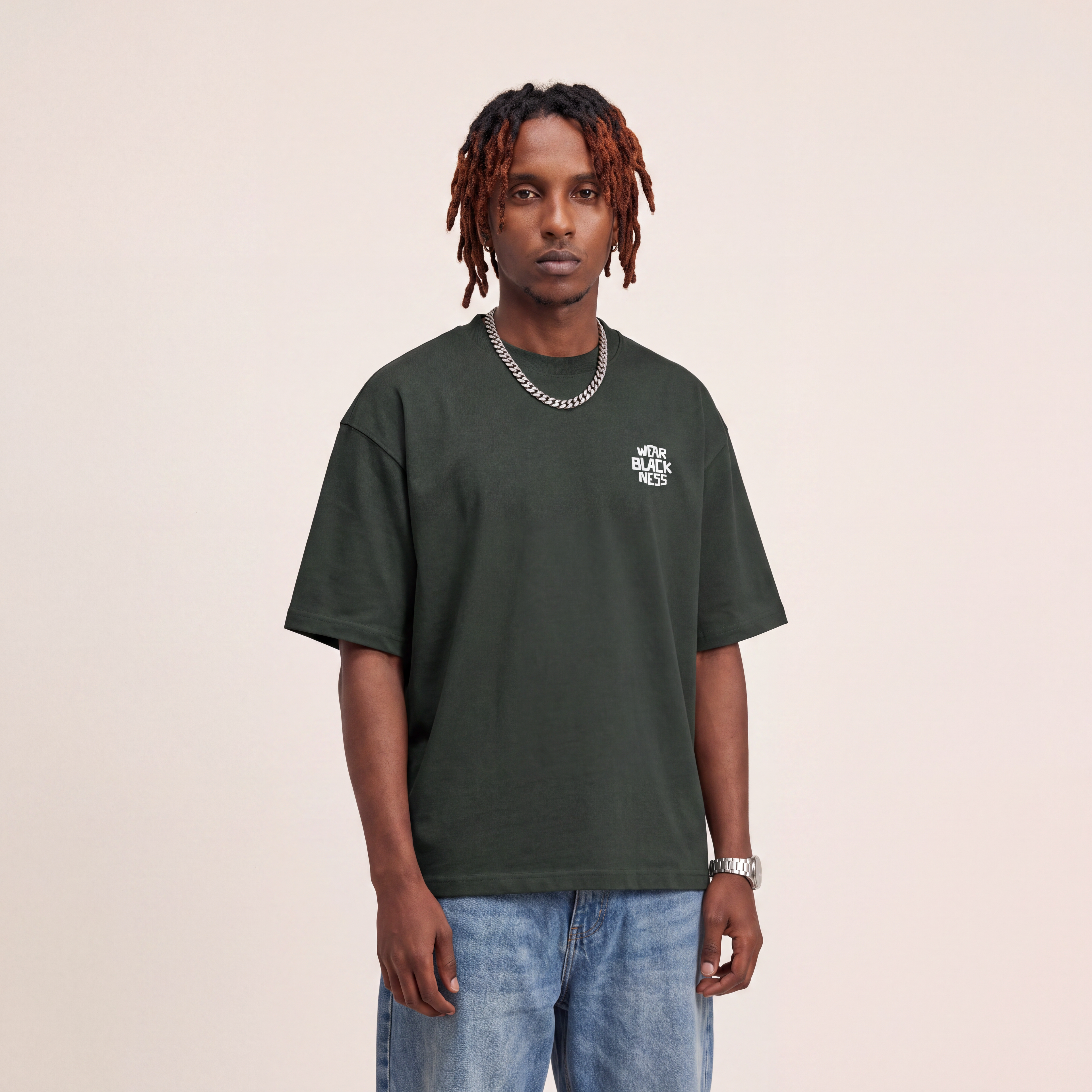 Wear Blackness Tee Green worn by model, front view with Wear Blackness chest print on warm ivory studio backdrop